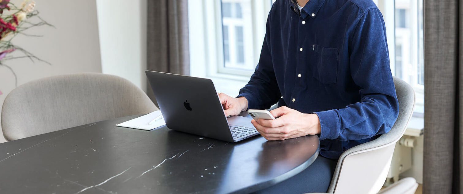 Mand foran computer med telefon i hånden